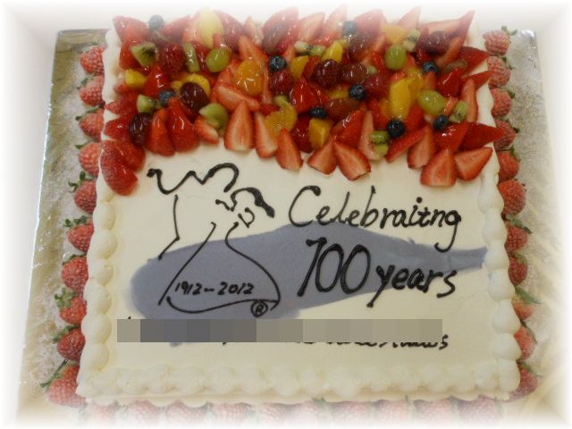 【ダンススクールの創立１００周年記念のケーキ】３０名様用のケーキに真ん中に大きく、デザインとロゴをかいて。周りをﾌﾙｰﾂで飾りました。