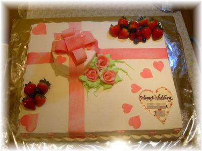 2009年10月のご注文です。５０名様用の大きなケーキに、片隅に小さく可愛いケーキを重ねて、大きなリボンをプレゼントのようにかけました。バラの花も飾って、シンプルながらも豪華なケーキになりました。
